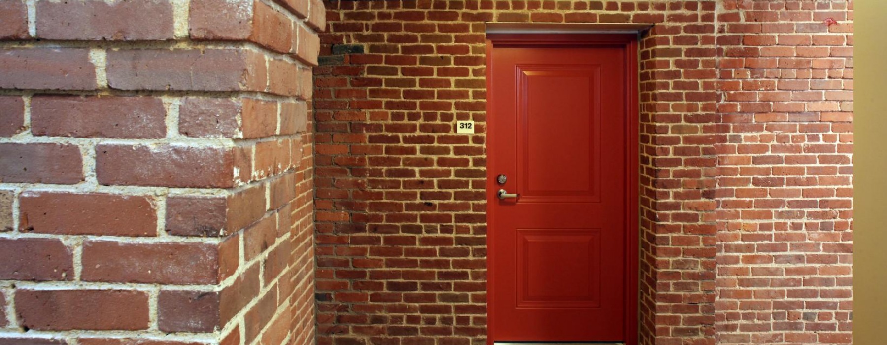 red door surrounded by red brick walls in hallway